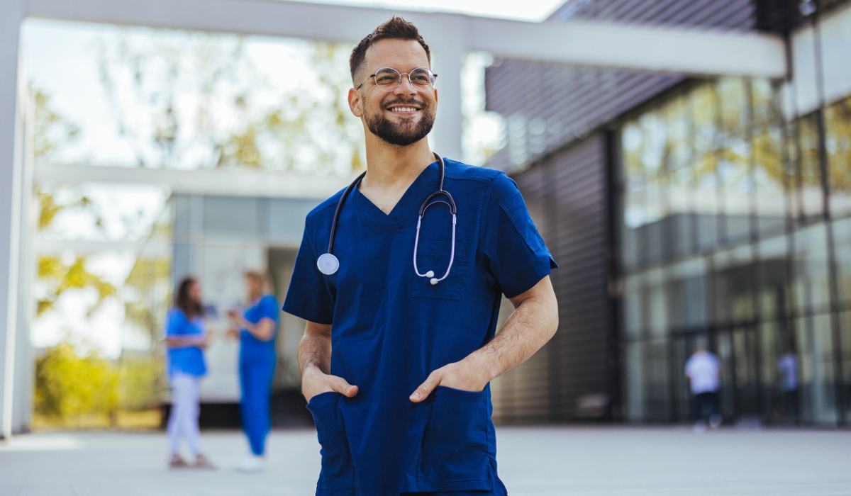 young medical practitioner standing with his arms crossed outside hospital