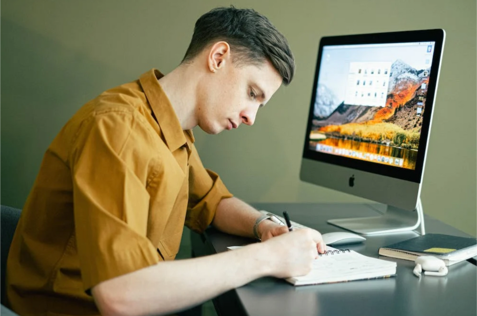 Man writing in notebook at laptop