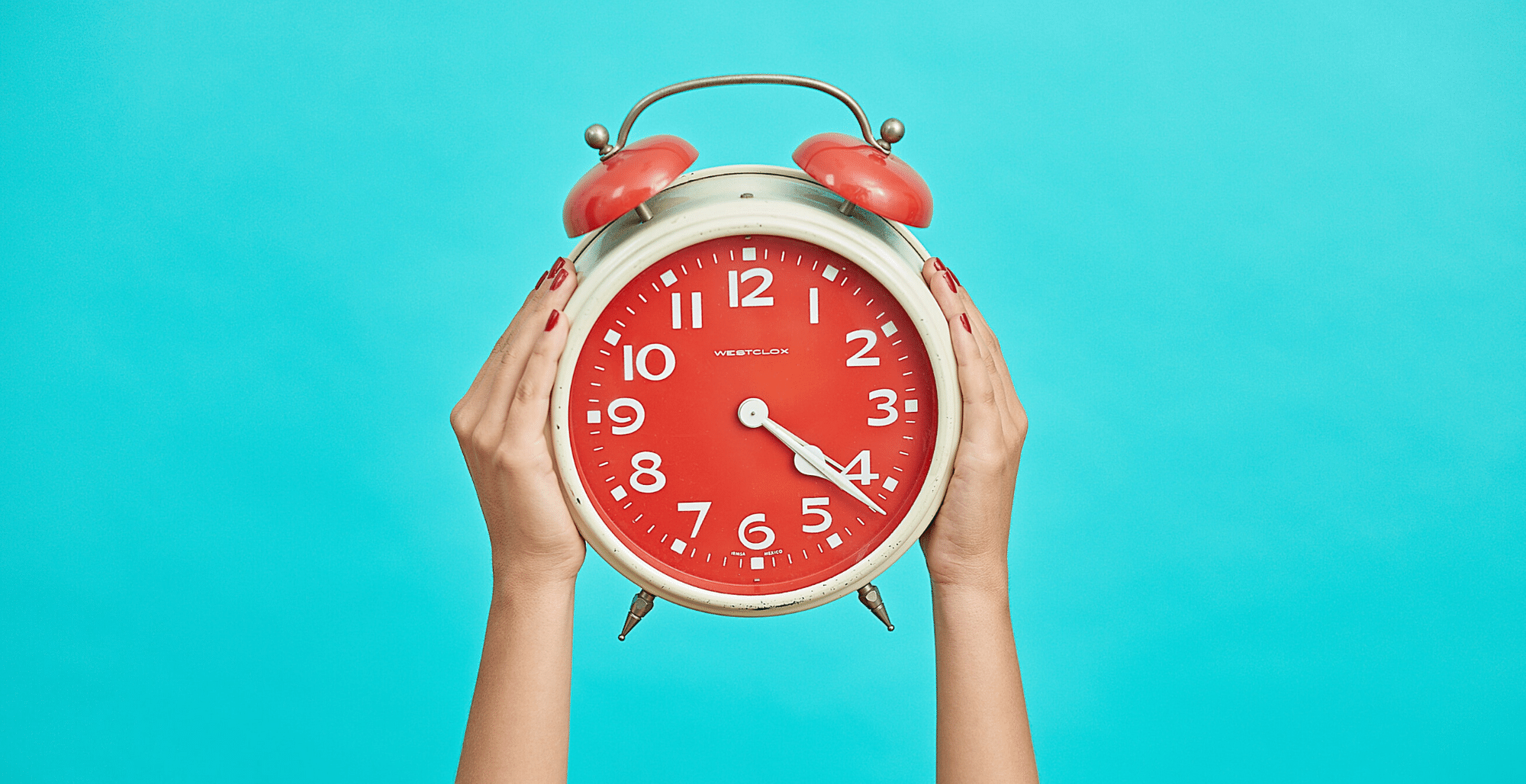 womans-hands-holding-up-red-alarm-clock